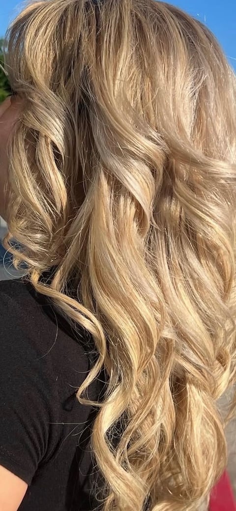Long wavy blonde hair with highlights in sunlight, styled with soft waves and dimension