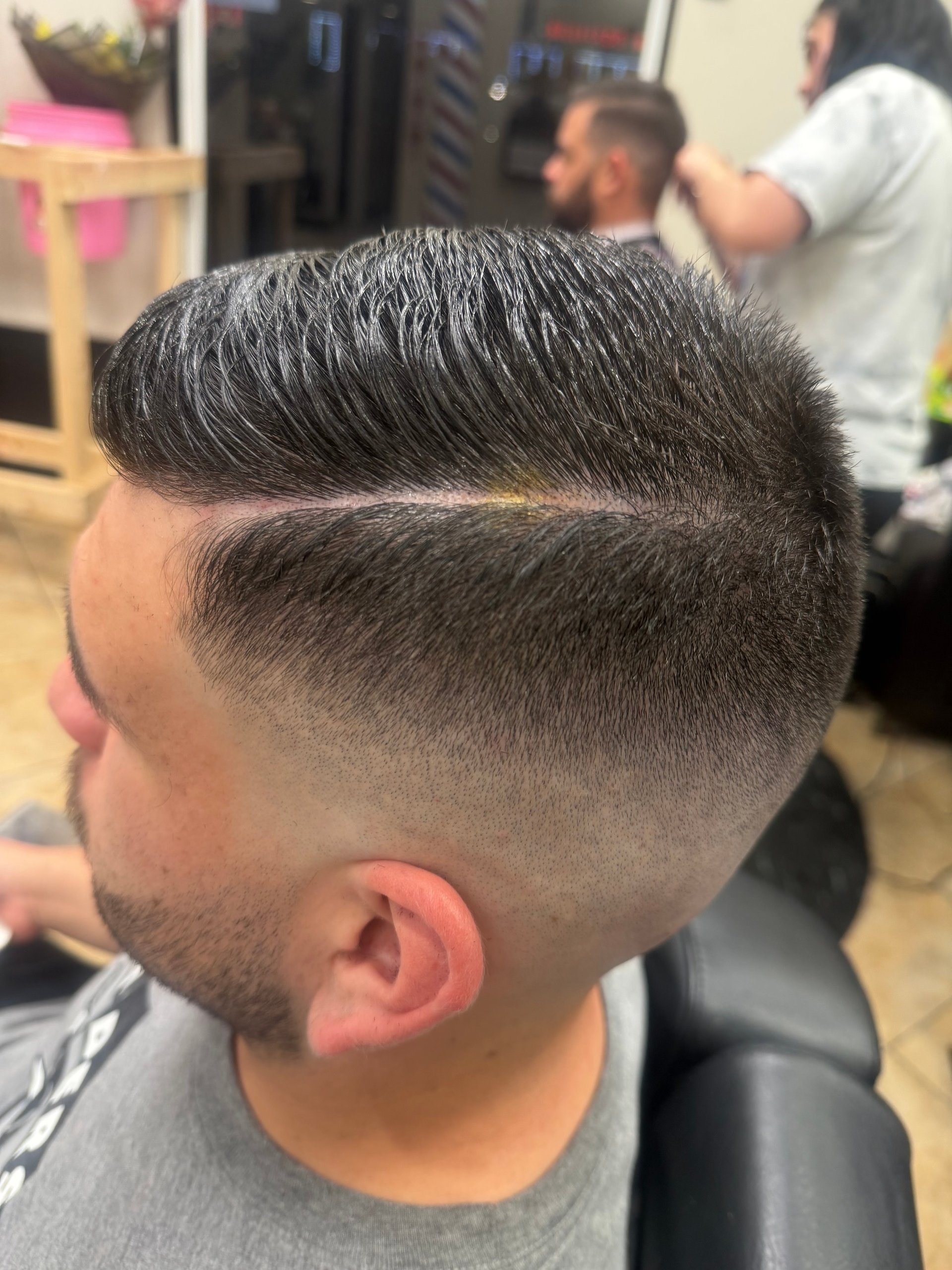 Close-up of a mans head showing a modern undercut hairstyle with a fade and pompadour-style top at a barbershop