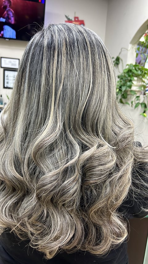 Back view of long wavy gray and blonde highlighted hair styled with voluminous waves in a salon setting