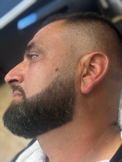 Profile view of a man with a full dark beard and short hair, looking to the left
