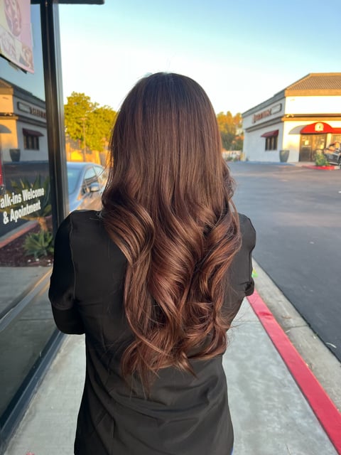 Woman with long brown hair viewed from behind standing at a shopping center parking lot at dusk