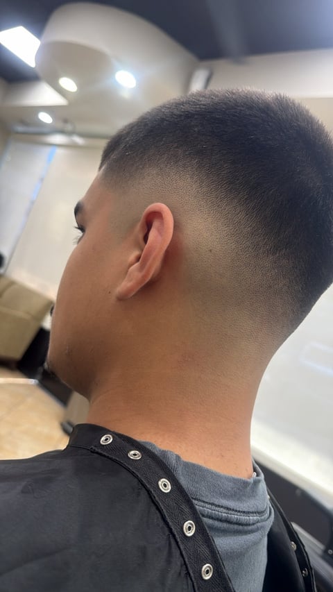 Side profile of a person with a short faded haircut in a barber shop with bright overhead lighting