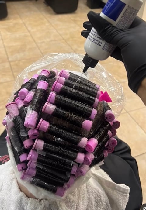 Person wearing black gloves applies product to head covered with pink and black hair rollers