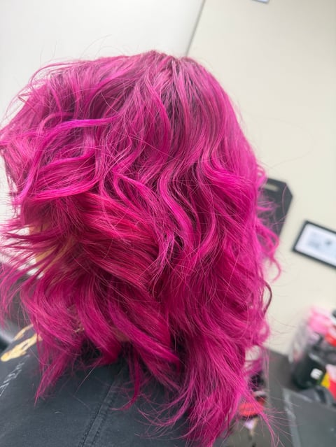 Back view of vibrant pink wavy hair with layered styling in an indoor salon setting