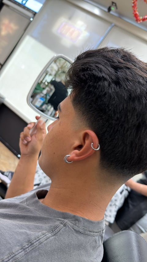 Person with dark hair and silver ear piercings holding up a phone, photographed from behind in an indoor setting